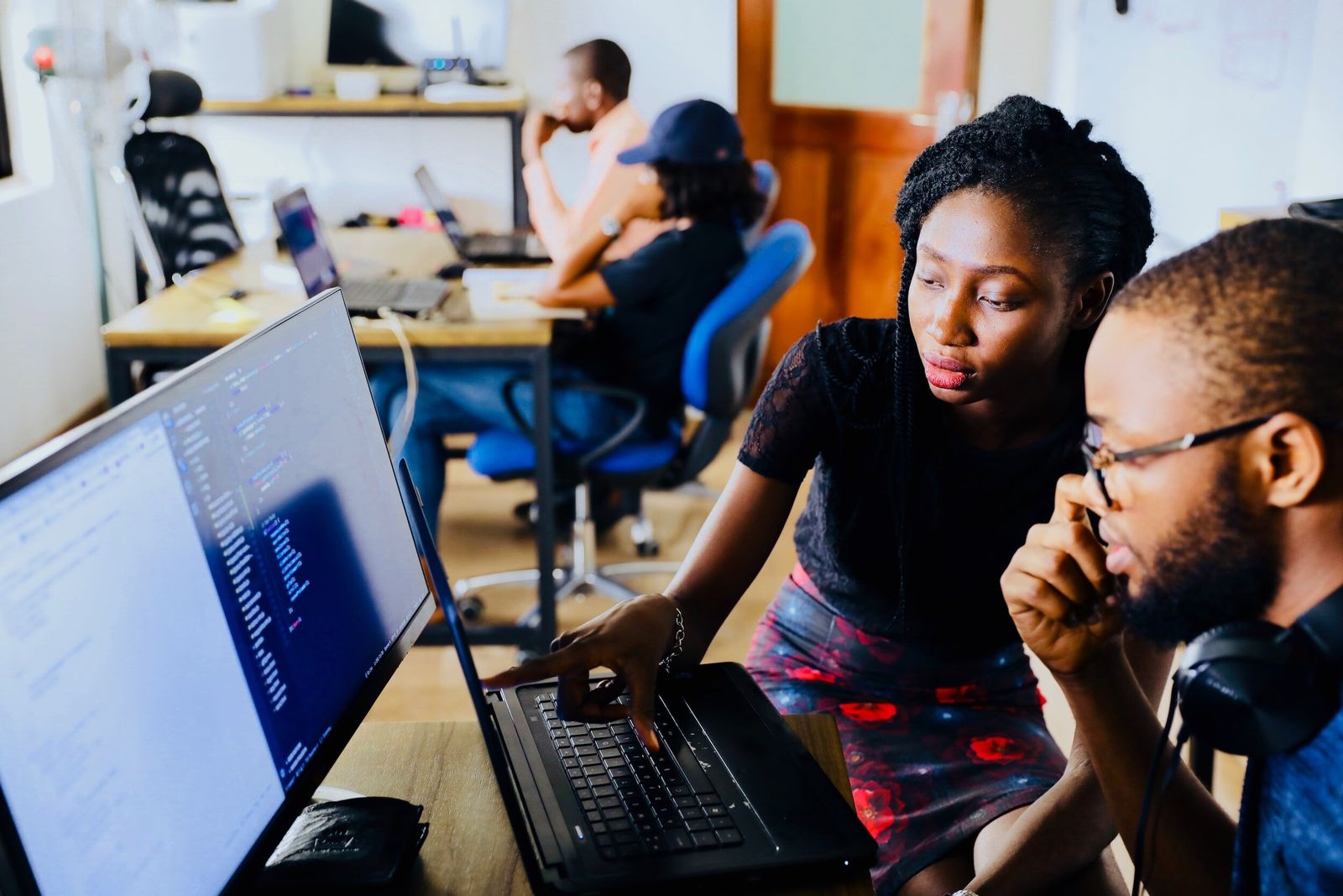 Two young Black professionals working together at a computer in a bright shared office
