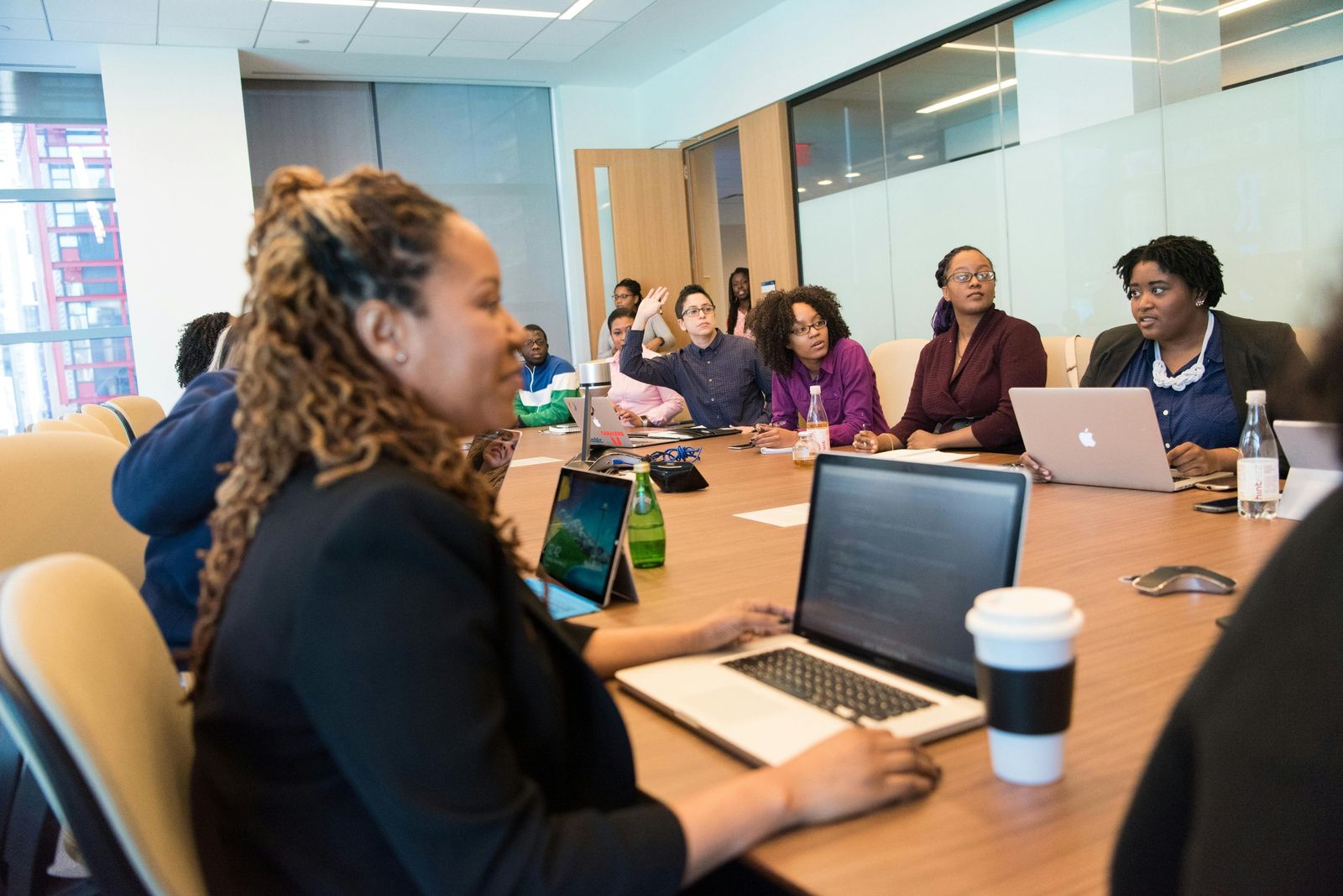 A Black woman working on a laptop during a group session around a boardroom table